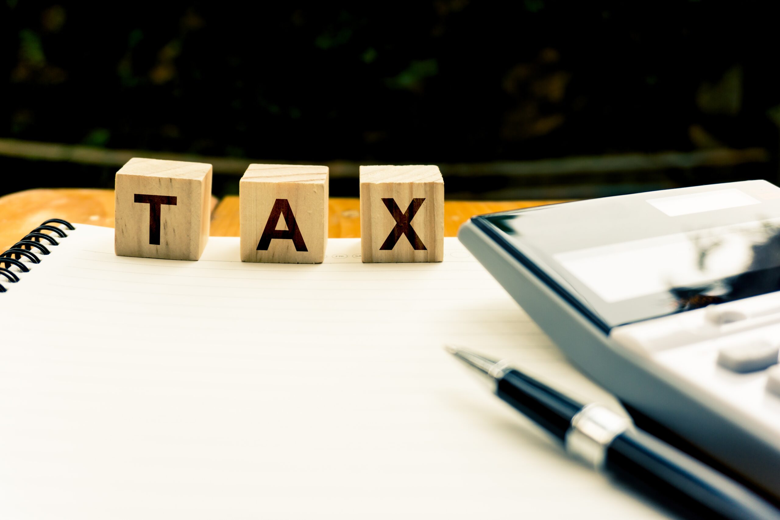 Taxation and Annual tax concept. A wooden block with message on blank note book, calculator and black pen with copy space. Depicts a income planning, annual tax deduction.